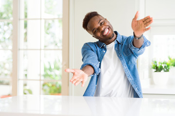 Handsome african american man at home looking at the camera smiling with open arms for hug. Cheerful expression embracing happiness.