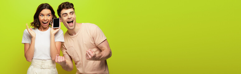 panoramic shot of happy young man showing yes gesture while standing near excited girl on green background