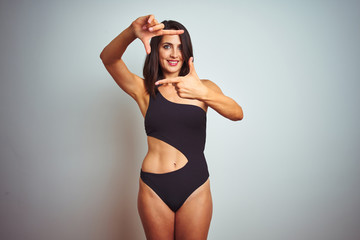 Beautiful woman wearing bikini swimwear over white isolated background smiling making frame with hands and fingers with happy face. Creativity and photography concept.