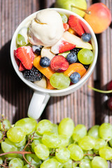 Bowl of healthy fresh fruit salad with ice cream on wooden background. Top view.