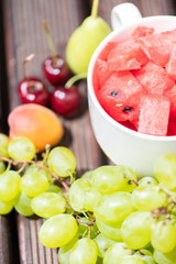 Bowl with delicious watermelon salad on wooden table with arranged fruit around.