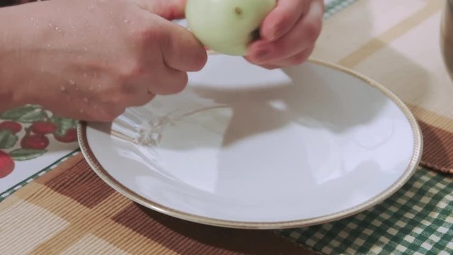 Adult woman cutting fresh apple with a knife and removing core from it. Cut apple parts and knife are left on a plate