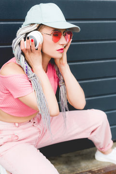 attractive stylish girl with dreadlocks and headphones posing near wall