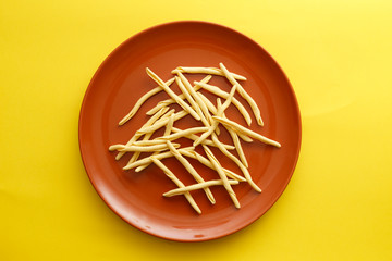 Raw strozzapreti pasta in a brown dish over a yellow background