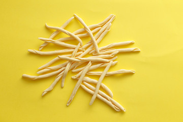 Raw strozzapreti pasta over a yellow background