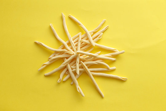 Raw strozzapreti pasta over a yellow background