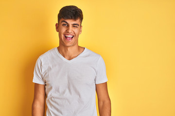 Young indian man wearing white t-shirt standing over isolated yellow background winking looking at the camera with sexy expression, cheerful and happy face.