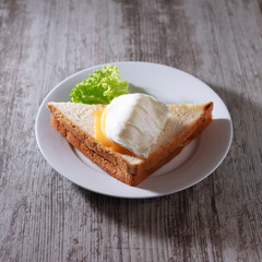 sandwich with poached egg and a leaf of lettuce on a white plate.