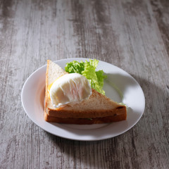 sandwich with poached egg and a leaf of lettuce on a white plate.