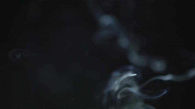 Threads of smoke rise in close view form soft, lengthy shapes. Smoke from incense or candle burning forms mystical shapes.
