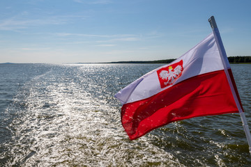 Polish flag suspended on the stern of a small inland ship. A vessel floating on a large lake in...