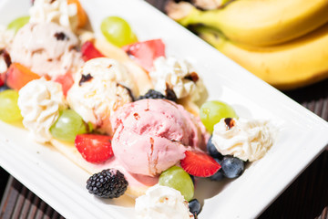 Plate of healthy fresh fruit salad with ice cream on the wooden background.