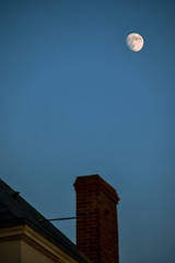 Chimney and roof unfocused, with the moon in the background. Concept of home and night.