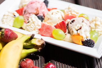 Plate of healthy fresh fruit salad with ice cream on the wooden background.