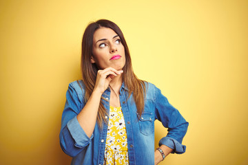 Young beautiful woman standing over yellow isolated background with hand on chin thinking about question, pensive expression. Smiling with thoughtful face. Doubt concept.