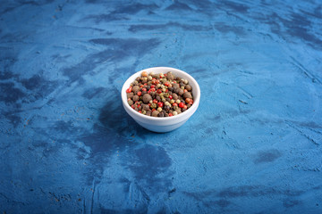 close up of mix of peppers in a pot against a blue stone background. spice