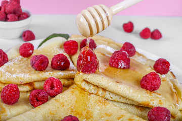 Close up pouring honey on pancakes which is on top with raspberries and honey drop. Pancakes are on the wooden table and pink background. Macro