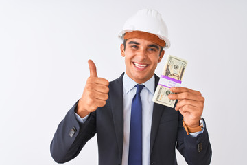 Young handsome architect man wearing helmet holding dollars over isolated white background happy with big smile doing ok sign, thumb up with fingers, excellent sign