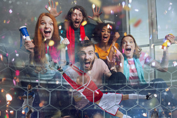 Happy friends of football fans watching soccer on tv and celebrating victory with falling confetti....