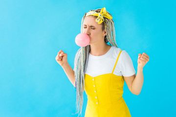 angry girl with dreadlocks and clenched fists blowing bubblegum isolated on turquoise
