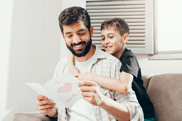 Happy father's day! Son congratulating dad and giving him a greeting card. Daddy and son smiling...