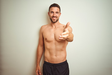 Fototapeta premium Young handsome shirtless man over isolated background smiling friendly offering handshake as greeting and welcoming. Successful business.