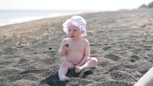 A yearling naked girl plays with stones on the sea beach