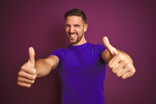 Young man wearing casual purple t-shirt over lilac isolated background approving doing positive gesture with hand, thumbs up smiling and happy for success. Winner gesture.