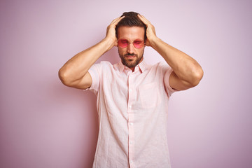 Handsome man wearing elegant summer shirt and sunglasses over pink isolated background suffering from headache desperate and stressed because pain and migraine. Hands on head.