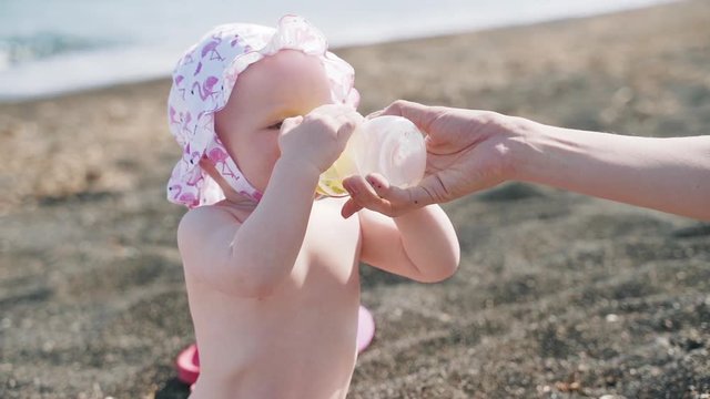 A little naked girl drinks from the bottle on the sea beach