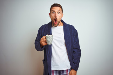 Man wearing comfortable pajamas and robe drinking cup of coffee over isolated background with surprise face pointing finger to himself