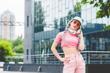 stylish girl in sunglasses with headphones posing and looking at camera