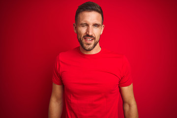Obraz premium Young handsome man wearing casual t-shirt over red isolated background winking looking at the camera with sexy expression, cheerful and happy face.