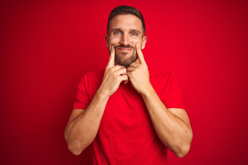 Obraz premium Young handsome man wearing casual t-shirt over red isolated background Smiling with open mouth, fingers pointing and forcing cheerful smile