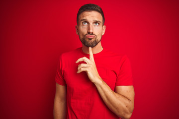 Young handsome man wearing casual t-shirt over red isolated background Thinking concentrated about...
