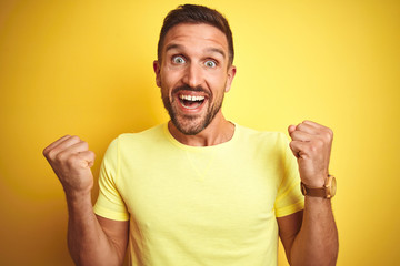 Young handsome man wearing casual yellow t-shirt over yellow isolated background celebrating surprised and amazed for success with arms raised and open eyes. Winner concept.