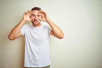 Young handsome man wearing casual white t-shirt over isolated background Trying to open eyes with fingers, sleepy and tired for morning fatigue