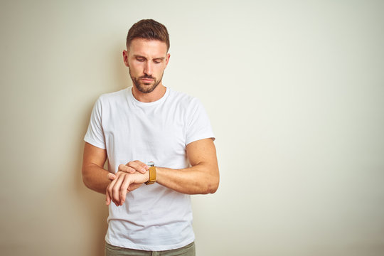 Young handsome man wearing casual white t-shirt over isolated background Checking the time on wrist watch, relaxed and confident