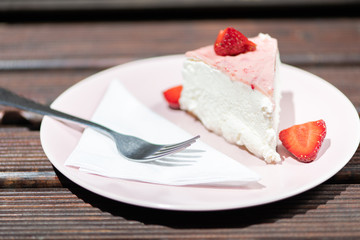 Slice of fresh strawberry tart on the pink plate with layered cream.