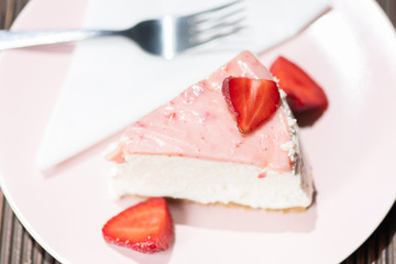 Slice of fresh strawberry tart on the pink plate with layered cream.