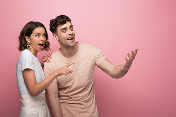 young, excited man and woman smiling and looking away on pink background