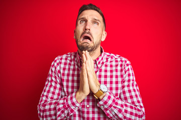 Young handsome man over red isolated background begging and praying with hands together with hope...