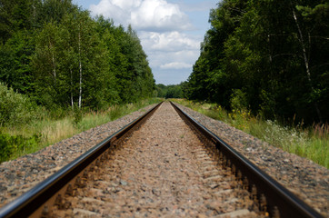 Railway on the background of green forest stretching into the distance. Two sleepers and rails on the gravel.