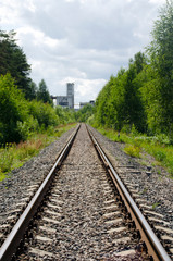 An abandoned railway that leads directly to an old industrial enterprise. Rails and sleepers on the background of the forest and the old building.