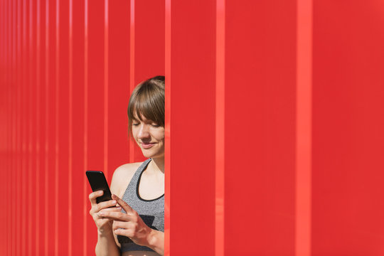 Sportswoman using phone in front of red wall