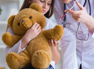 Woman female doctor examining little cute girl with toy bear
