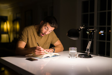 Young handsome man studying at home, reading a book at night