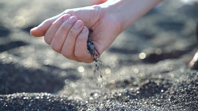 The black volcanic sand and pebbles crumbles from hand in slowmo