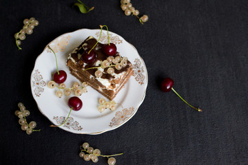 Top view of a slide of chocolate cake with a cherry on a white plate on a black background