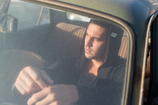 Young man sitting in a broken car on a scrapyard